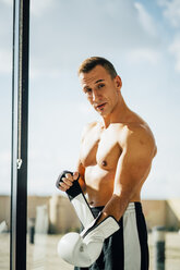 Portrait of boxer preparing to fight putting on boxing glove at the window - OCMF00128