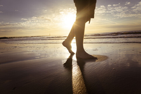 Netherlands, Cadzand-Bad, legs of teenage boy walking on the beach at twilight stock photo