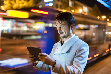 Porträt eines lächelnden Geschäftsmannes, der nachts auf der Straße ein digitales Tablet betrachtet - DIGF05571