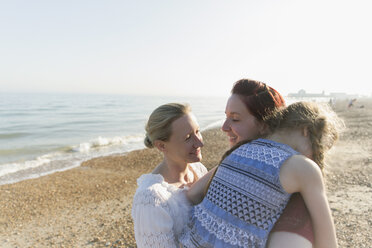 Lesbian couple hugging daughter on sunny beach - CAIF22252