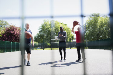 Aktive ältere Männer spielen Basketball im sonnigen Park - CAIF22264