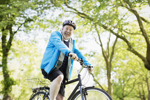 Porträt lächelnder aktiver älterer Mann beim Fahrradfahren im Park - CAIF22265