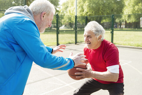 Aktive ältere Männer spielen Basketball im sonnigen Park, lizenzfreies Stockfoto