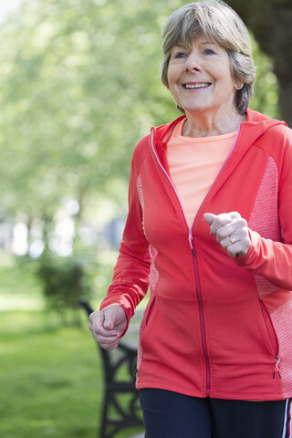 Lächelnde aktive ältere Frau beim Laufen im Park, lizenzfreies Stockfoto