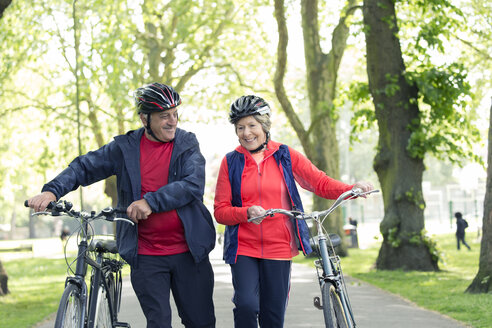 Active senior couple walking bikes in park - CAIF22287