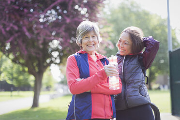 Portrait confident active senior female runner friends drinking water in park - CAIF22292