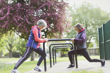 Active senior female runners stretching legs in park - CAIF22304