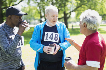 Aktive ältere Männer, die ein Sportrennen beenden und im sonnigen Park Kaffee trinken - CAIF22311