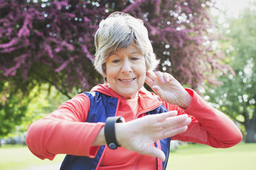 Aktive ältere Läuferin überprüft ihre Smartwatch im Park - CAIF22312