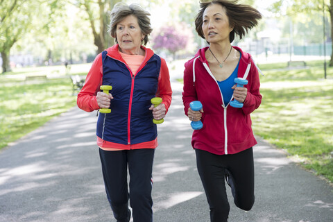 Aktive ältere Freundinnen joggen mit Handgewichten im Park, lizenzfreies Stockfoto