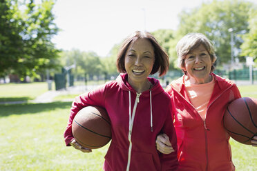 Porträt glücklicher, aktiver älterer Frauen, die im sonnigen Park Basketball spielen - CAIF22316