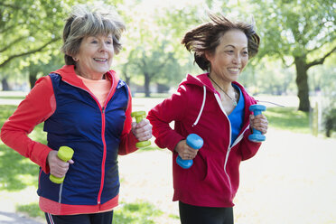 Aktive ältere Freundinnen joggen mit Handgewichten im Park - CAIF22322