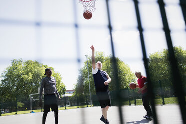 Aktive ältere Männer spielen Basketball im sonnigen Park - CAIF22323