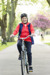 Portrait active senior woman riding bike in park - CAIF22324