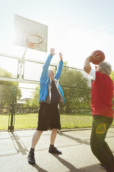 Aktive ältere Männer spielen Basketball im sonnigen Park - CAIF22331