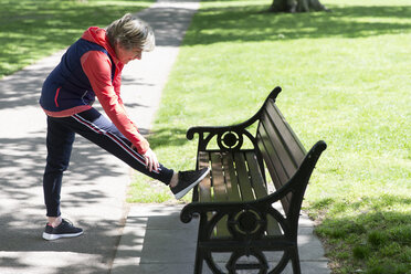Aktive ältere Frau streckt ihr Bein auf einer Parkbank - CAIF22332