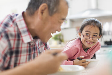 Smiling grandfather and granddaughter eating at table - CAIF22336