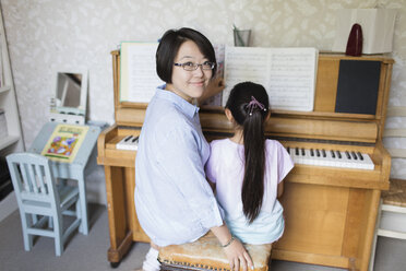 Porträt lächelnde Mutter sitzend mit Tochter beim Klavierspielen - CAIF22342