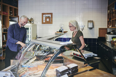 Customer smiling while showing seafood at retail display to saleswoman in deli - MASF09758