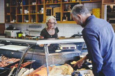 Customer showing seafood at retail display to saleswoman in deli - MASF09760