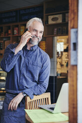 Verkäuferin lächelt, während sie in einem Feinkostladen mit dem Handy telefoniert - MASF09764