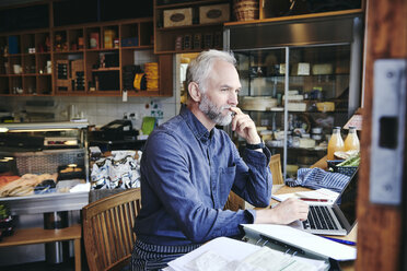 Thoughtful salesman using laptop at table in deli - MASF09767