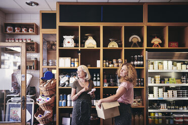 Female colleagues looking away while standing by rack in deli - MASF09778