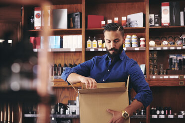 Verkäufer beim Auspacken eines Kartons, während er an einem Regal im Feinkostladen steht - MASF09782