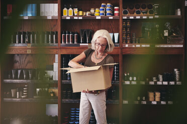 Senior saleswoman unpacking cardboard box against rack in deli - MASF09787