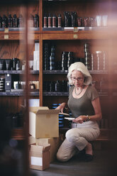 Senior saleswoman reading paper while unpacking box in deli - MASF09789