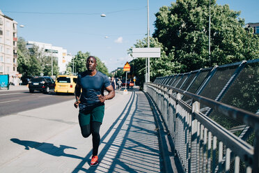 Männlicher Sportler in voller Länge beim Joggen auf dem Gehweg an einer Brücke in der Stadt - MASF09840