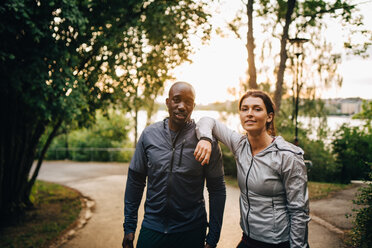 Portrait of confident male and female athletes standing on road in park - MASF09841