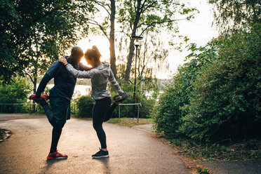 Full length of male and female athletes stretching legs while standing on road in park - MASF09842