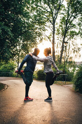 Full length of male and female athletes stretching legs while standing on road in park - MASF09843