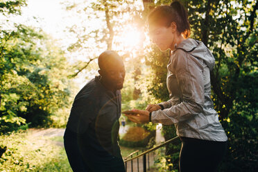 Young female athlete showing mobile phone to sportsman while standing in park - MASF09851