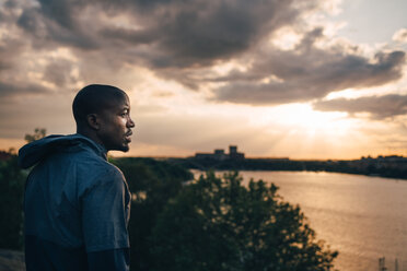 Male athlete looking away while standing on hill against sky during sunset - MASF09855