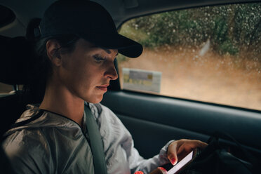 Eine Sportlerin benutzt ein Mobiltelefon während einer Autofahrt in der Regenzeit - MASF09868