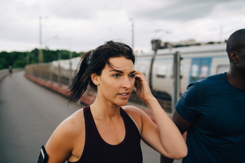 Junge Sportlerin schaut weg, während sie mit einem männlichen Freund auf einem Steg joggt - MASF09887