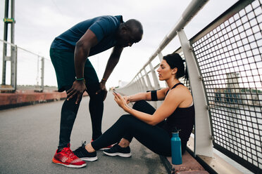 Eine Sportlerin zeigt einem Sportler auf einem Steg ihr Mobiltelefon - MASF09890