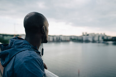 Seitenansicht eines männlichen Sportlers, der auf einer Fußgängerbrücke über dem Meer steht und auf die Stadt blickt, gegen den Himmel - MASF09892