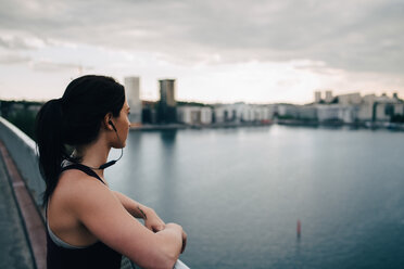 Side view of female athlete looking at city while standing on footbridge over sea - MASF09893