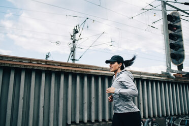 Young sportswoman jogging by fence on footbridge in city - MASF09902