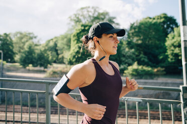 Selbstbewusste Sportlerin hört Musik beim Joggen auf einer Brücke in der Stadt - MASF09912