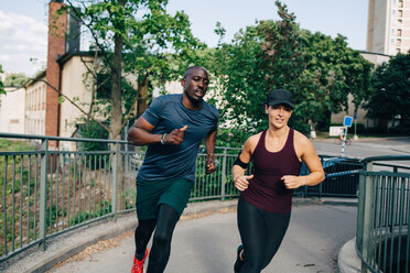 Determined male and female friends jogging on bridge in city - MASF09913