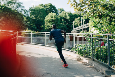 Rear view of sportsman jogging on footbridge in city - MASF09915