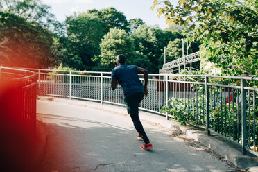 Rückansicht eines Sportlers, der auf einer Fußgängerbrücke in der Stadt joggt - MASF09915