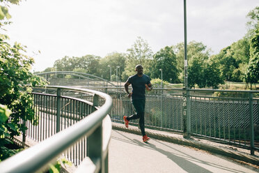 Voller Länge der Mitte erwachsenen Sportler joggen auf Fußgängerbrücke in der Stadt während des sonnigen Tages - MASF09916