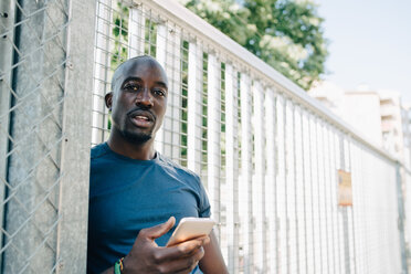 Portrait of sportsman using mobile phone while leaning on railing at bridge - MASF09917