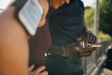 Midsection of sportsman showing mobile phone to female athlete while standing on bridge - MASF09918