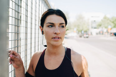 Junge Sportlerin schaut weg, während sie auf einer Brücke Musik über In-Ear-Kopfhörer hört - MASF09920